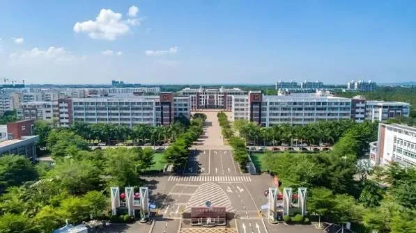 Gedung kampus bata merah dengan menara jam dan taman.